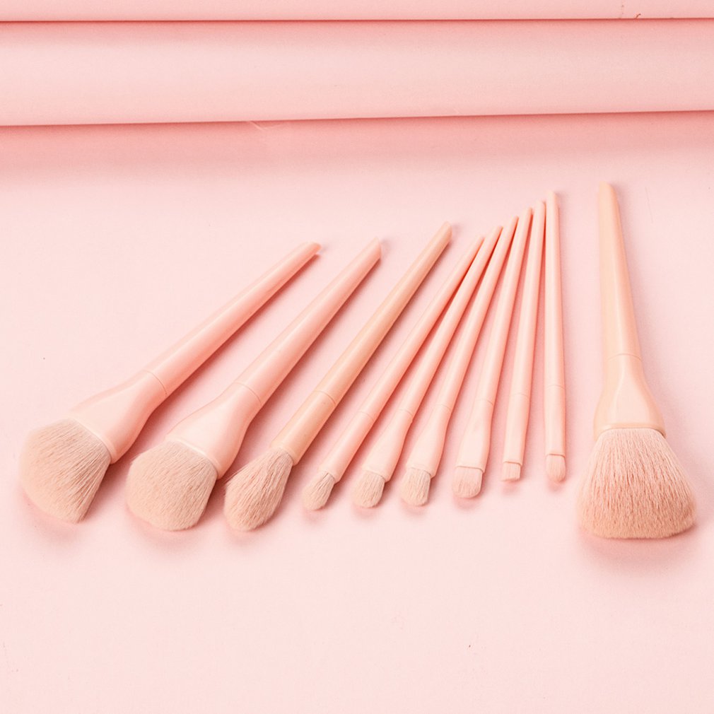 Set of various light pink makeup brushes arranged on a matching pink background.