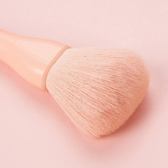 Close-up of a soft, light pink makeup powder brush on a matching pink background.
