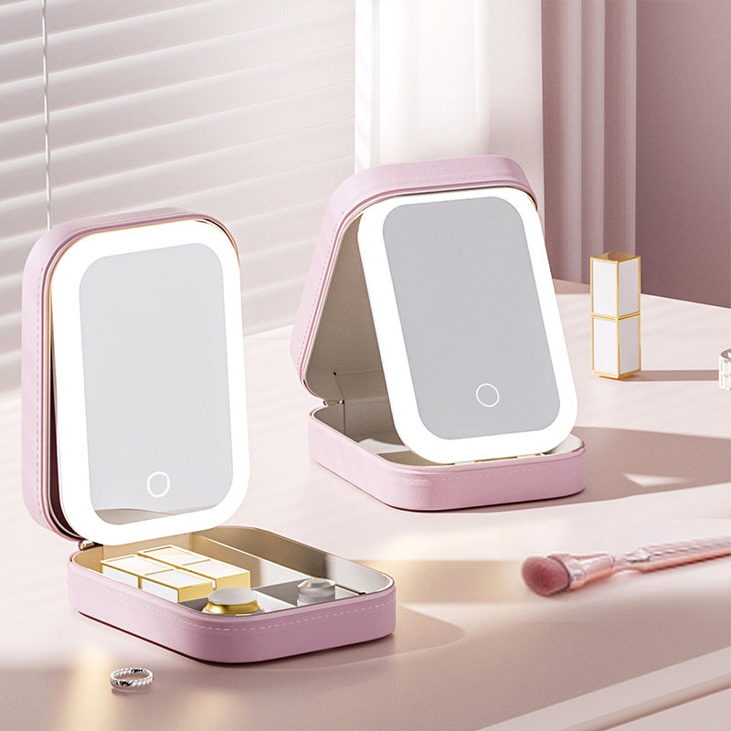 Two pink portable makeup compacts with LED mirrors and storage compartments on a white table.