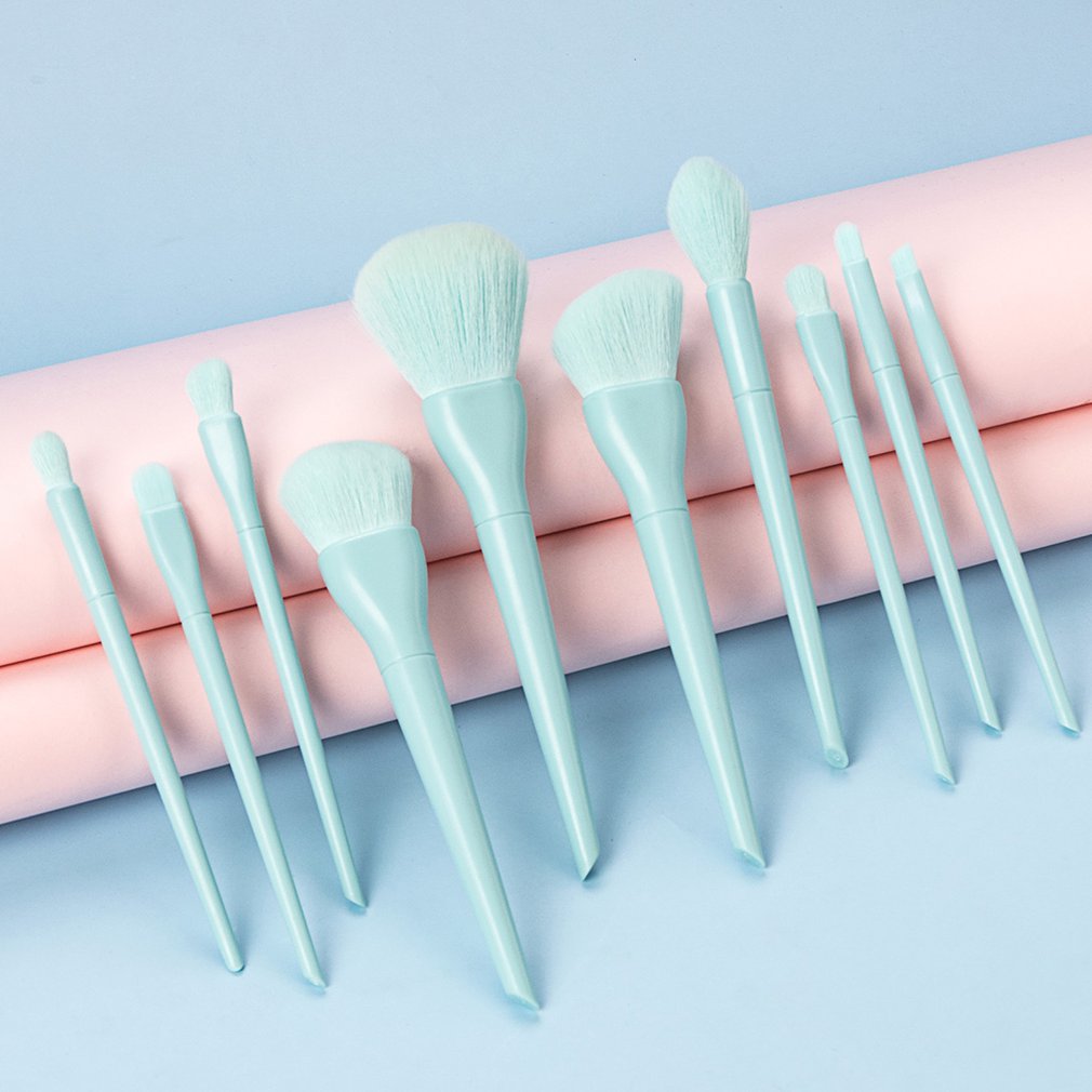 Set of light blue makeup brushes arranged on a pink background